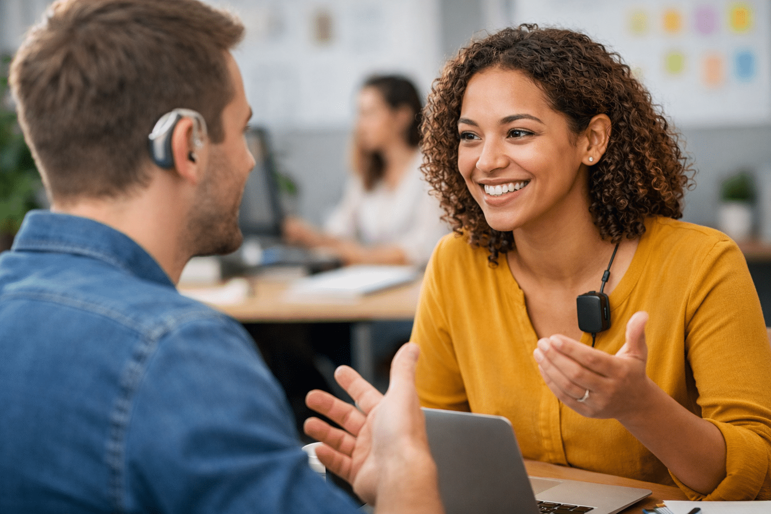 Salarié malentendant avec prothèse auditive en situation de travail, échange avec une collègue en entreprise.
